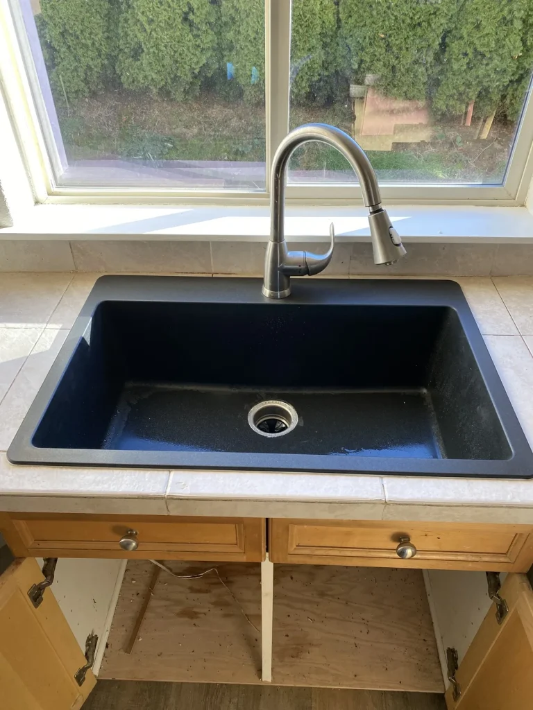 Black granite composite kitchen sink with a stainless pull-down faucet after a remodel