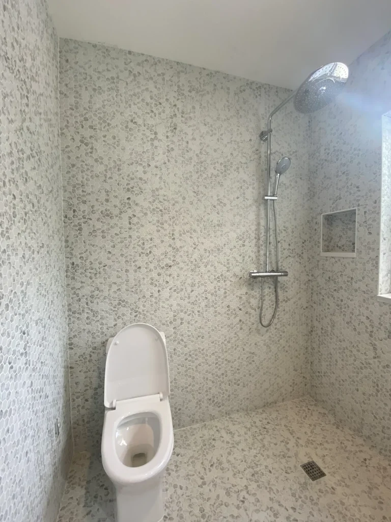 Walk-in shower wrapped in marble mosaic tile with a chrome rain shower column