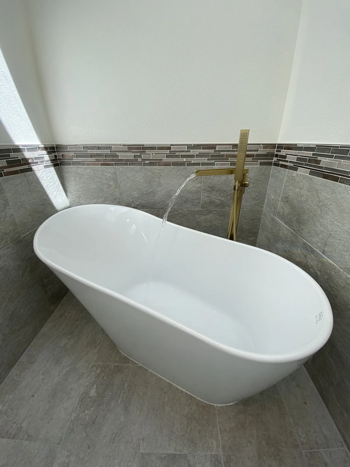 Freestanding slipper tub filling from a brushed gold floor-mount tub filler