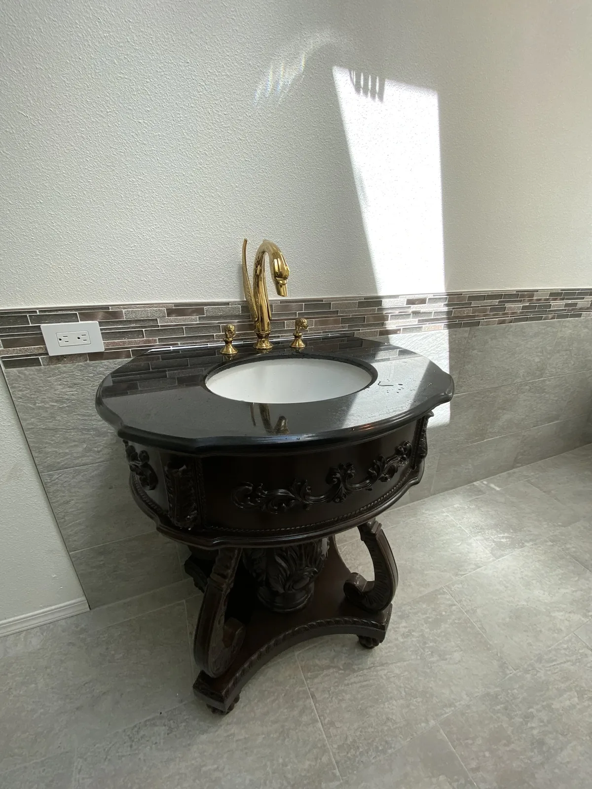 Restored carved wood pedestal vanity with black granite top and gold swan-neck faucet