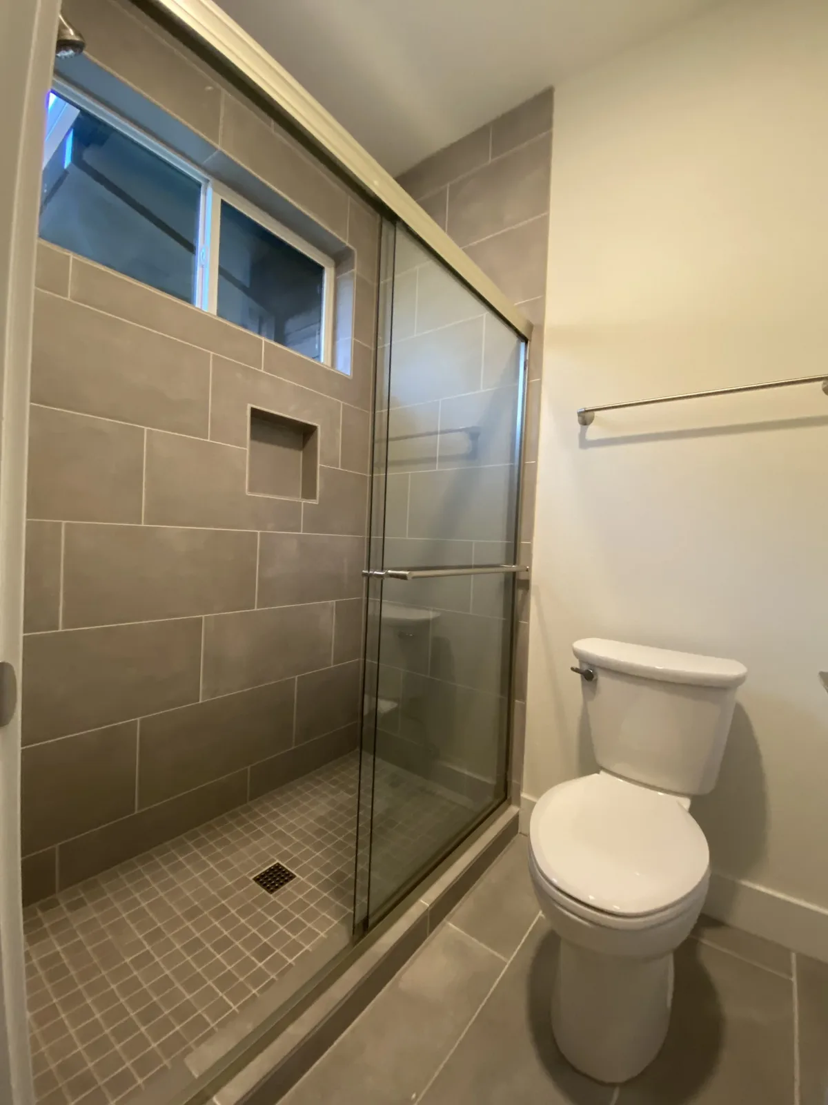Walk-in shower with large-format greige tile, mosaic pan, and glass slider