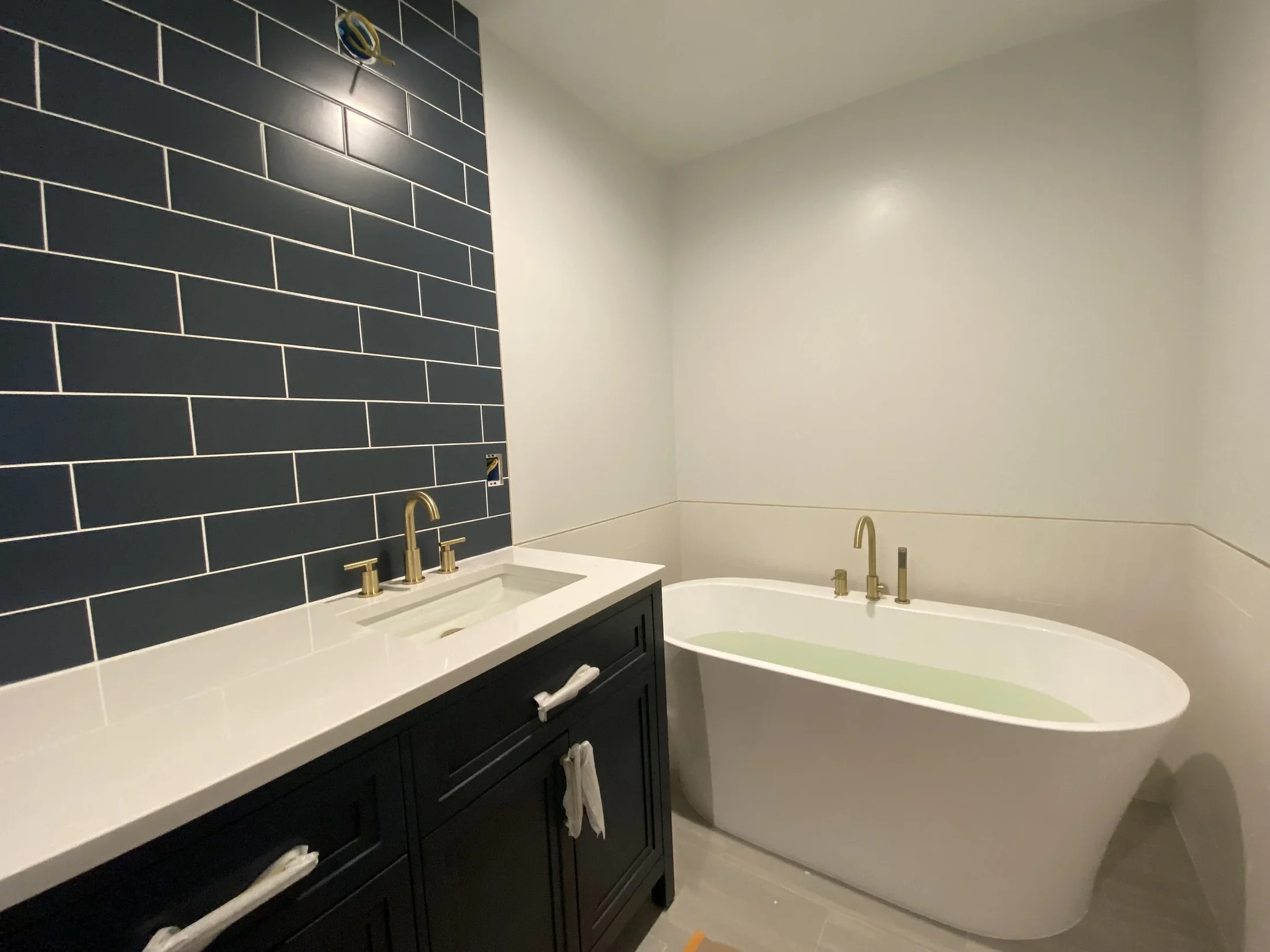 Completed bathroom remodel by Panda Plumbing with navy tile, freestanding tub, and brushed gold fixtures