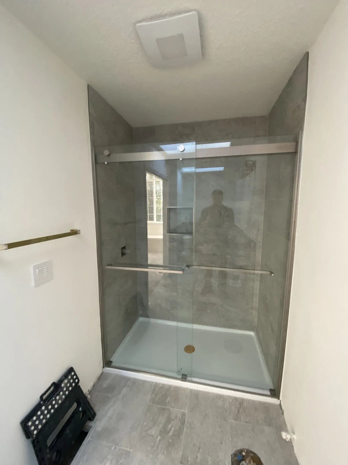New sliding glass shower enclosure with gray large-format tile and low-threshold pan during installation